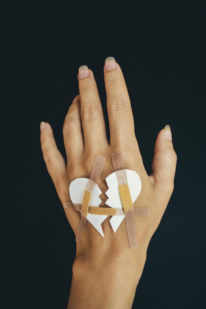 A hand with a paper broken heart mended by band-aids on a dark background.