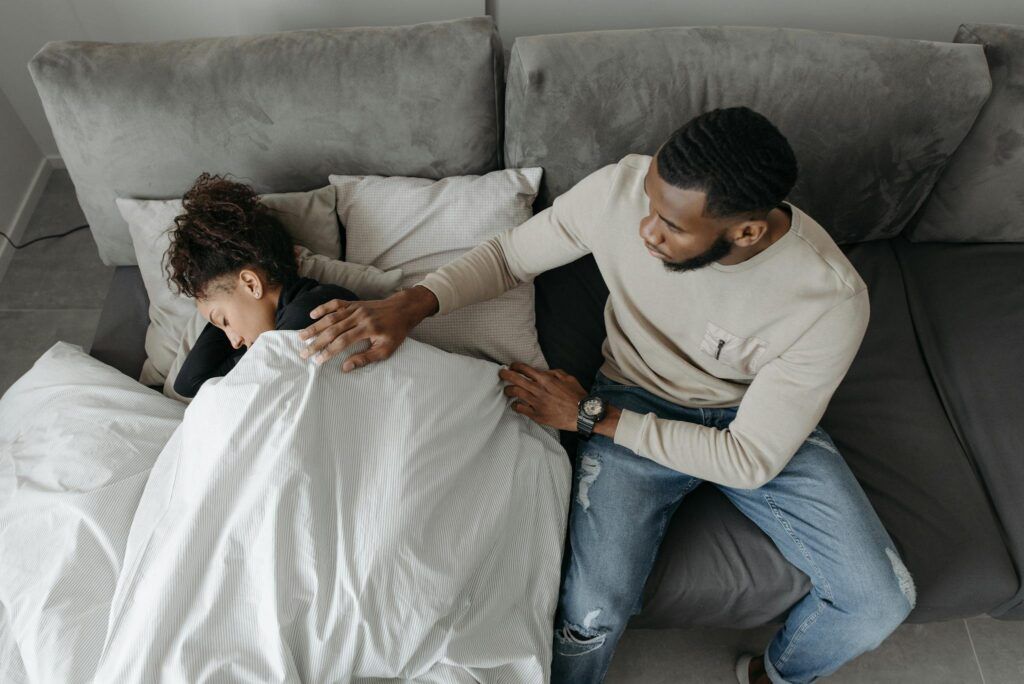 A man tenderly cares for a woman resting on a couch, illustrating compassion and support.
